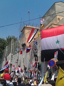 ７月11日、ダマスカスの米大使館の入り口に巨大なシリア国旗を掲げるアサド大統領の支持者 （C）EPA=時事